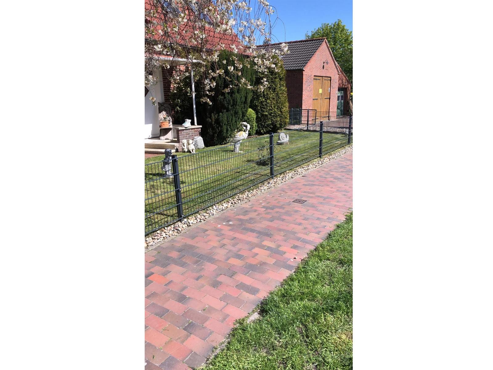 Pflasterweg führt zu einer Villa mit Gartenzaun und Blühsträuchern.