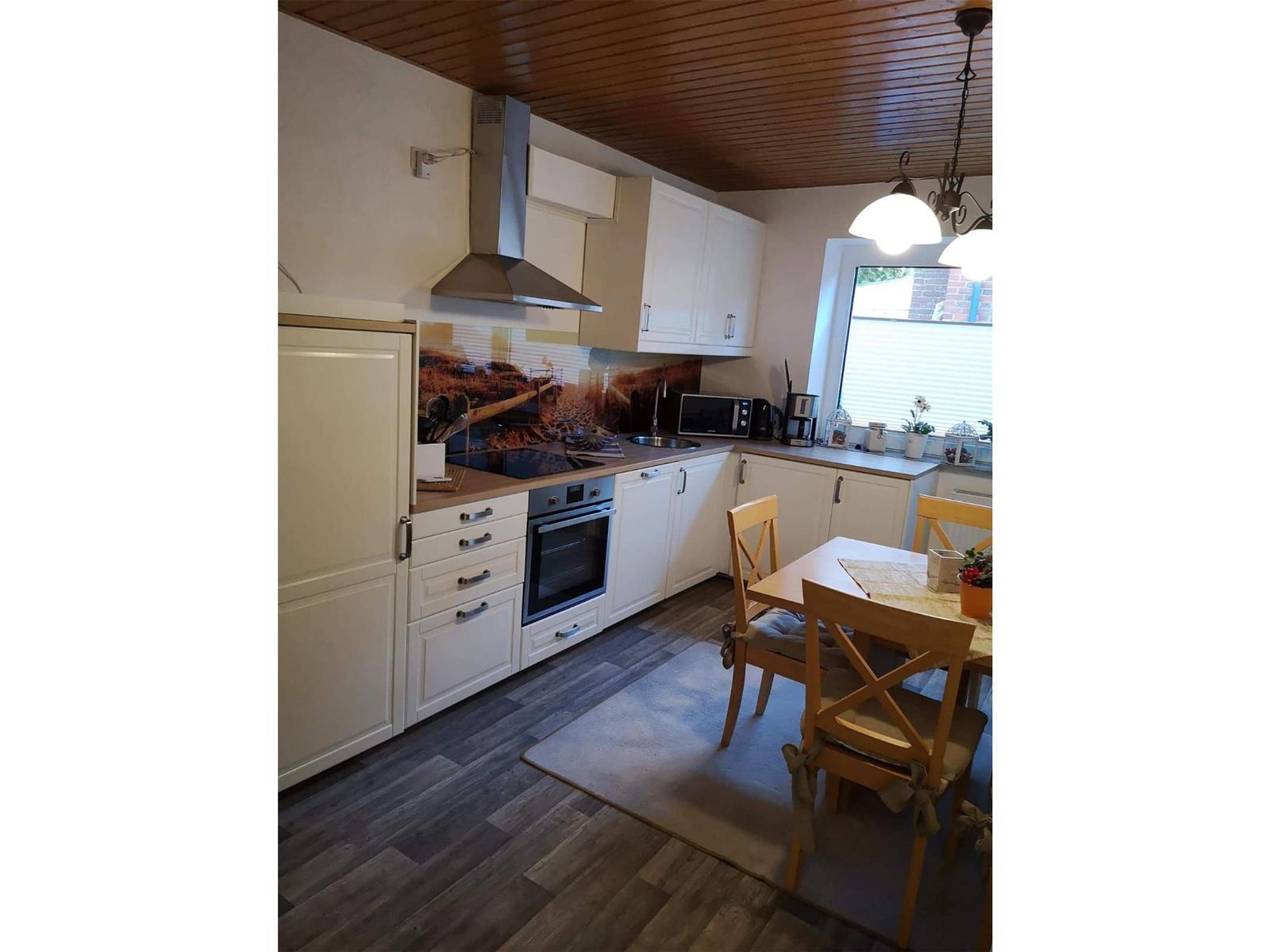 Küche mit Essbereich, weißen Schränken, Holzfußboden und Fenster mit Jalousie.