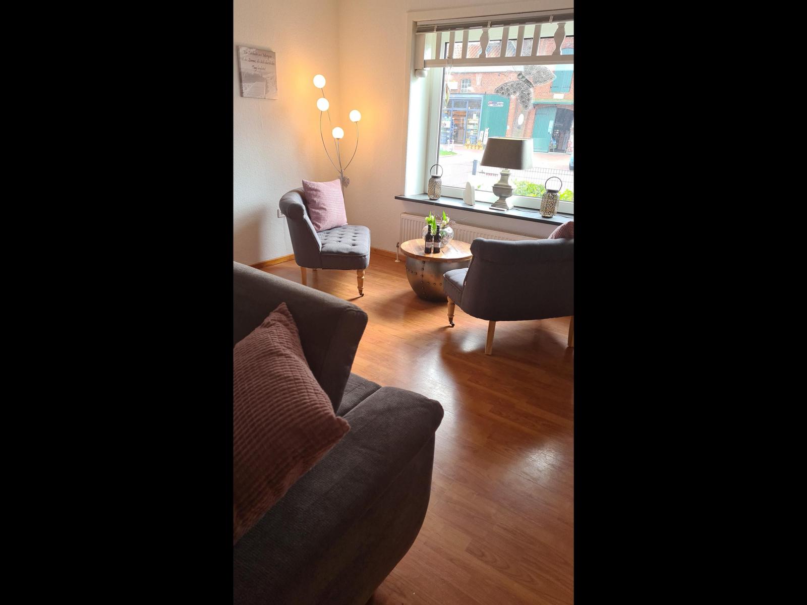 Wohnzimmer mit Sofa, zwei Sesseln und Holzboden. Fenster mit Blick auf Straße.