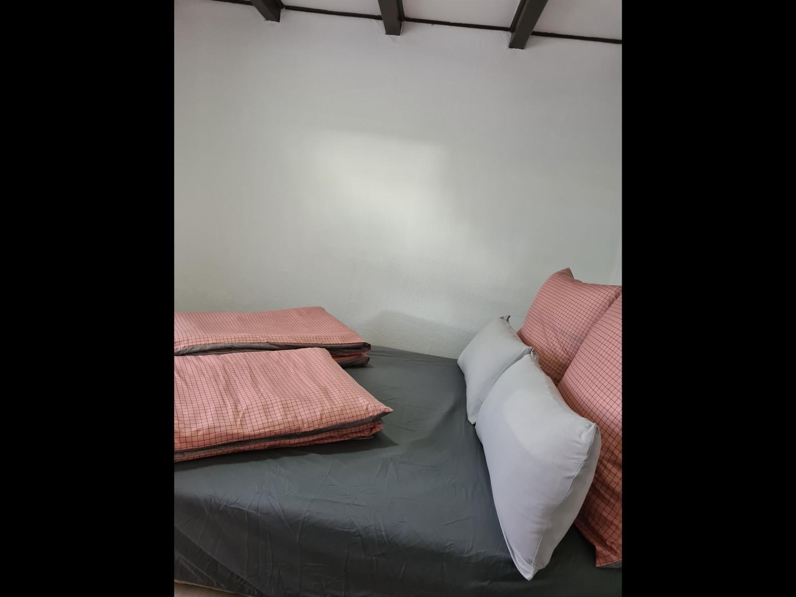 Ein Bett mit grauer Bettwäsche und rosa Kissen. Weiße Wände und dunkle Balken an der Decke.