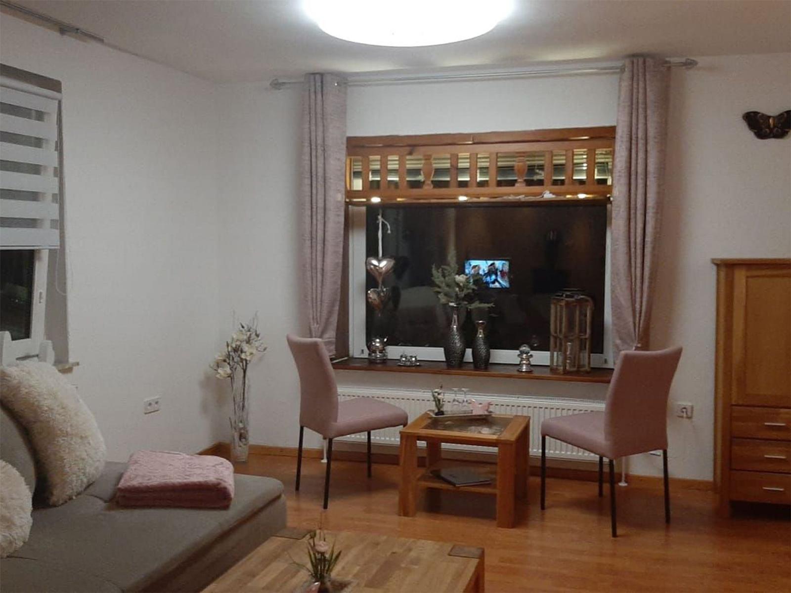 Wohnzimmer mit Sofa, zwei Stühlen, Tisch und Fenster mit Vorhängen.