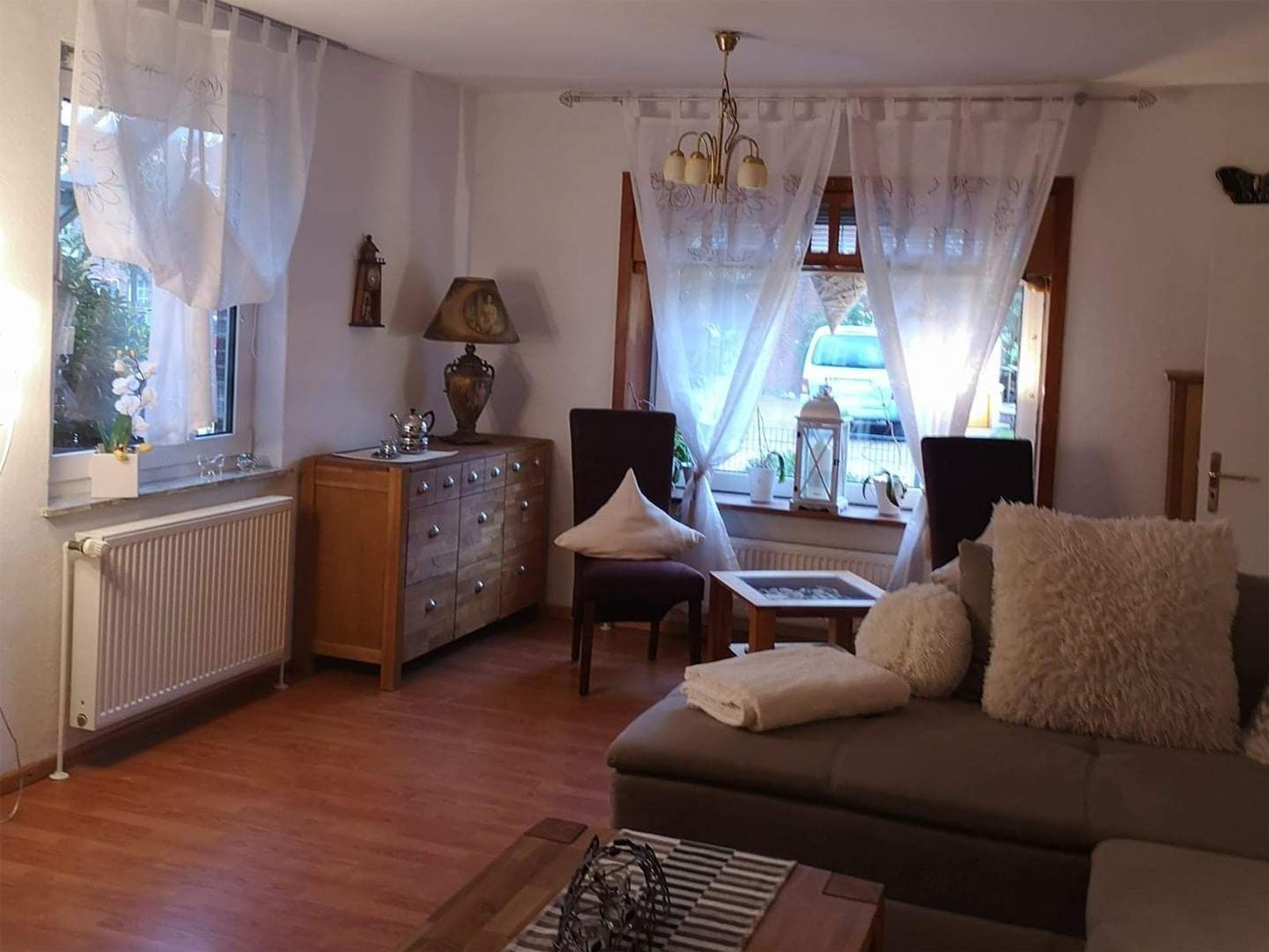 Wohnzimmer mit Sofa, Stühlen, Holzboden und Fenstern mit Vorhängen.