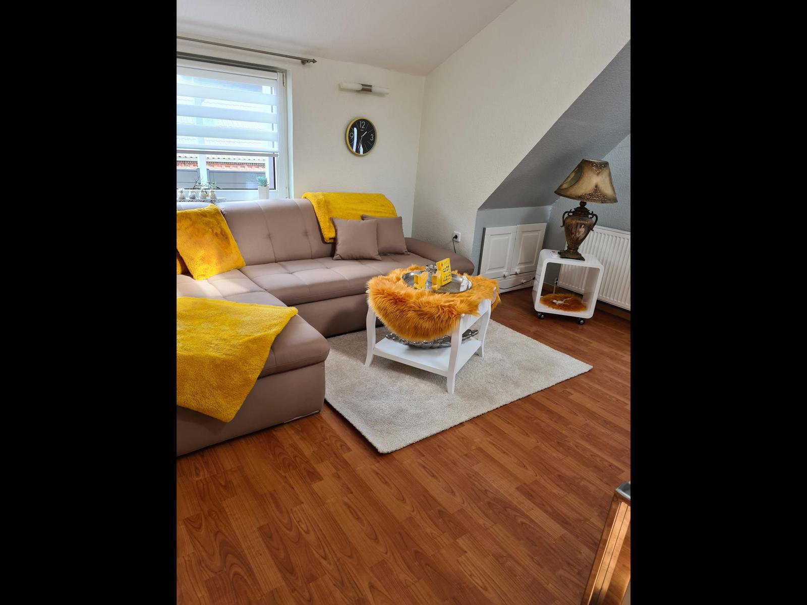 Wohnzimmer mit braunem Sofa, gelben Kissen und Holzboden.