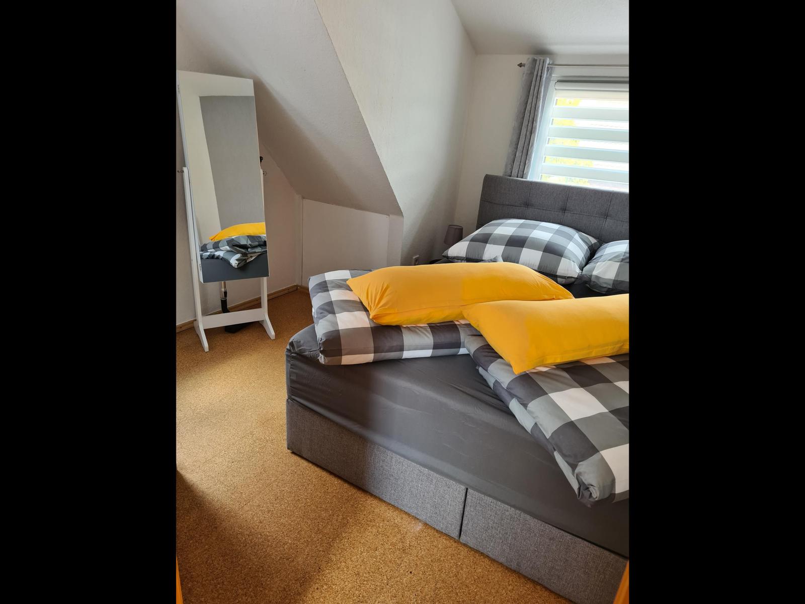 Schlafzimmer mit Doppelbett, Spiegel und Fenster mit Jalousie.
