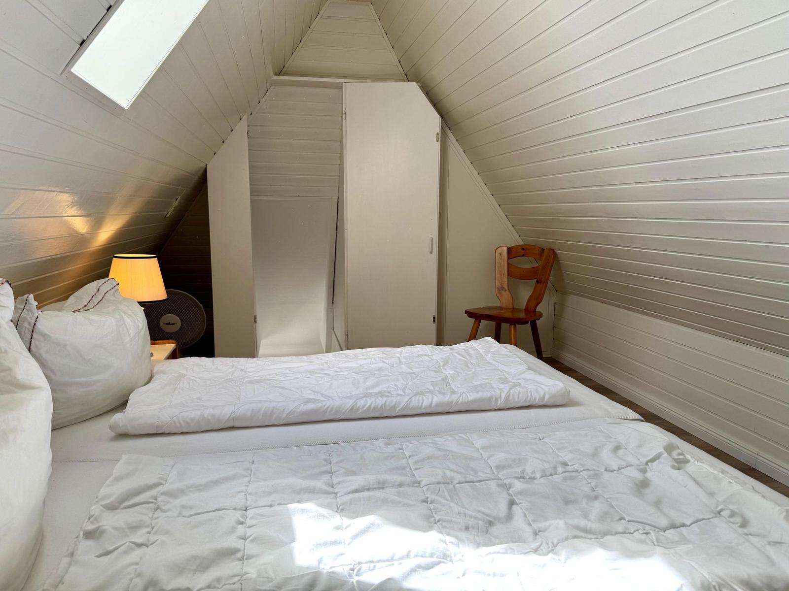 Bedroom with sloped ceiling, white bed, and wooden chair.