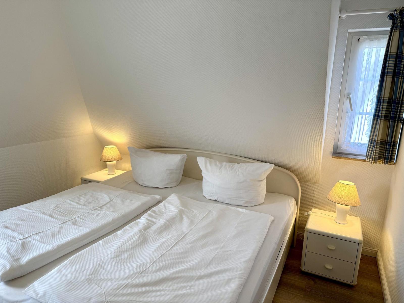 Bedroom with double bed, two nightstands, and lamp. Window with curtain.