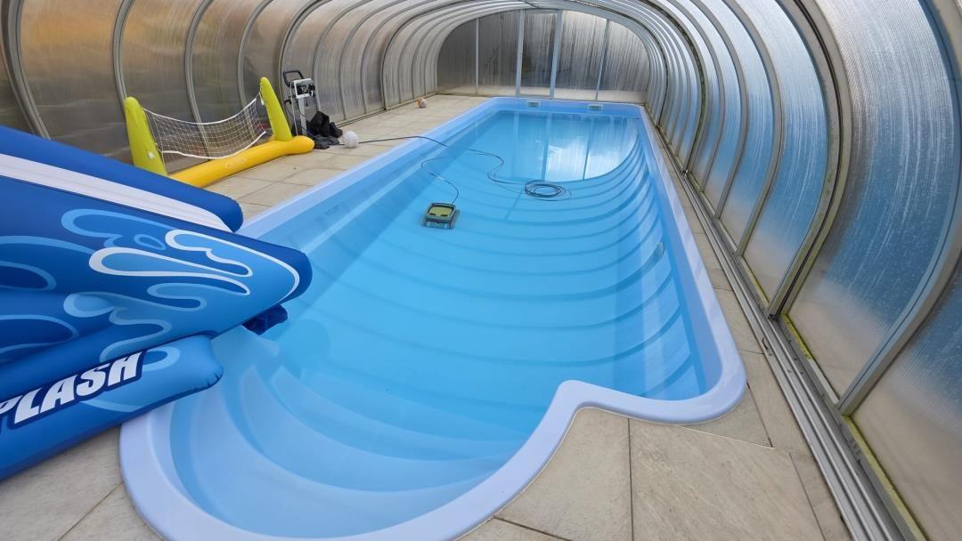 Ein langer Schwimmbadbereich unter einer transparenten Plane mit blauem Wasser und einem aufblasbaren Spielgerät.