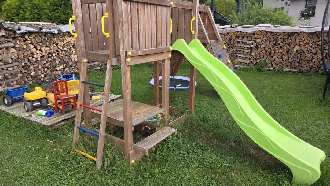 Holzspielplatz mit grünem Rutschbrett und Kinderspielzeug im Garten.