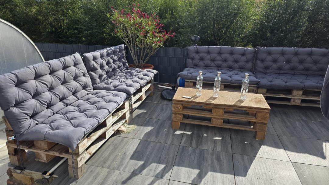 Terrasse mit zwei Palettensofas und Tisch aus Paletten. Hintergrund: Hecke und Pflanze.
