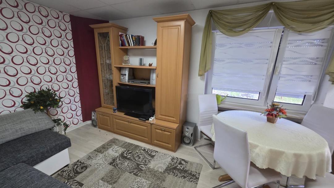 Wohn- und Essbereich mit TV, Esstisch und Bücherregal.