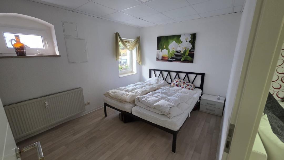 Schlafzimmer mit Doppelbett, zwei Fenstern und Wandbild.
