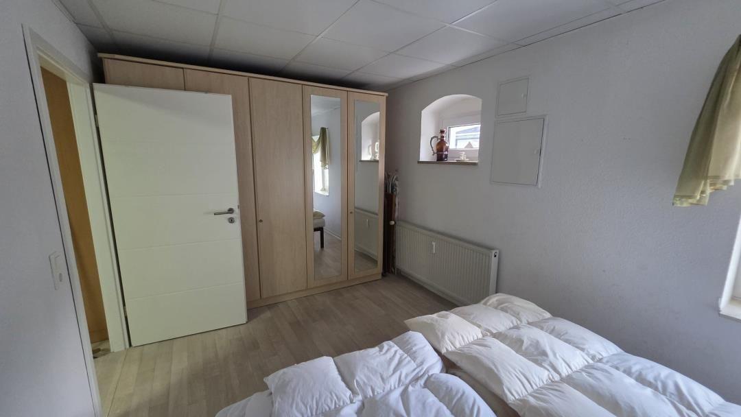 Schlafzimmer mit Bett, Kleiderschrank und Fenster.