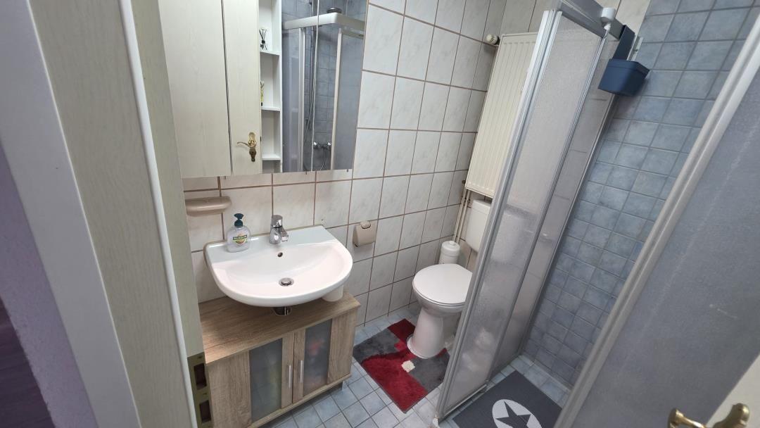 Badezimmer mit Waschbecken, Toilette und Dusche. Fliesenwand und Holzschrank.