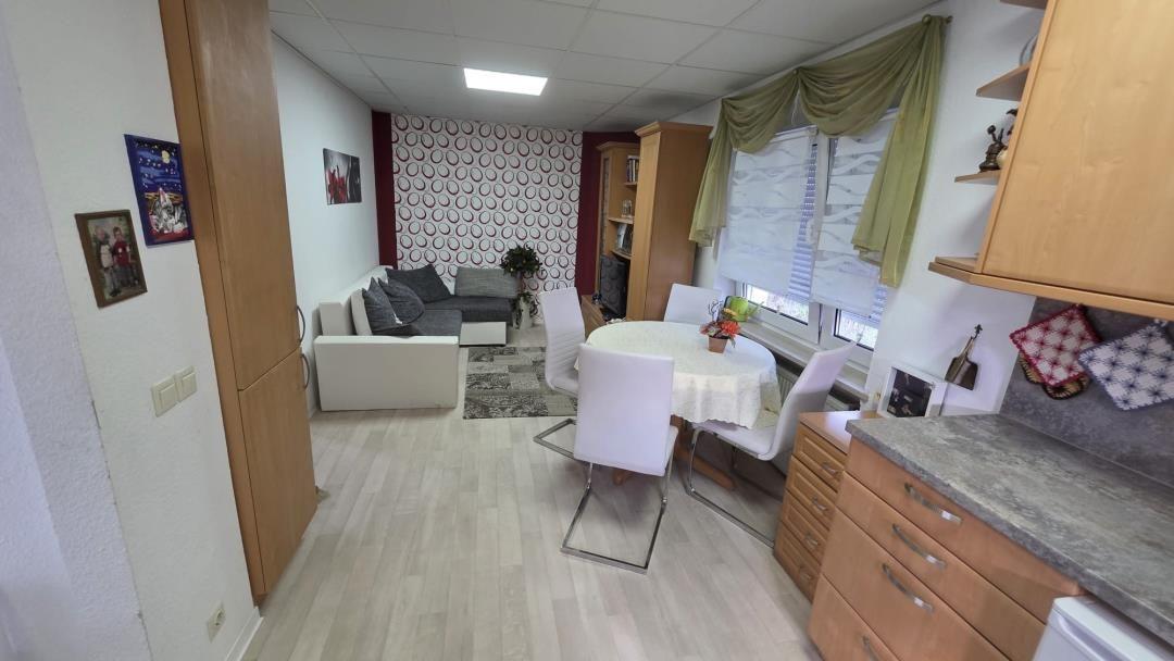 Wohnzimmer mit Sofa, Esstisch und Küche. Holzboden und Fenster mit Vorhängen.