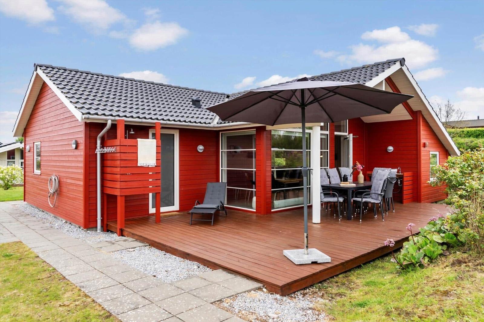 Red vacation home with terrace, umbrella, and garden furniture.