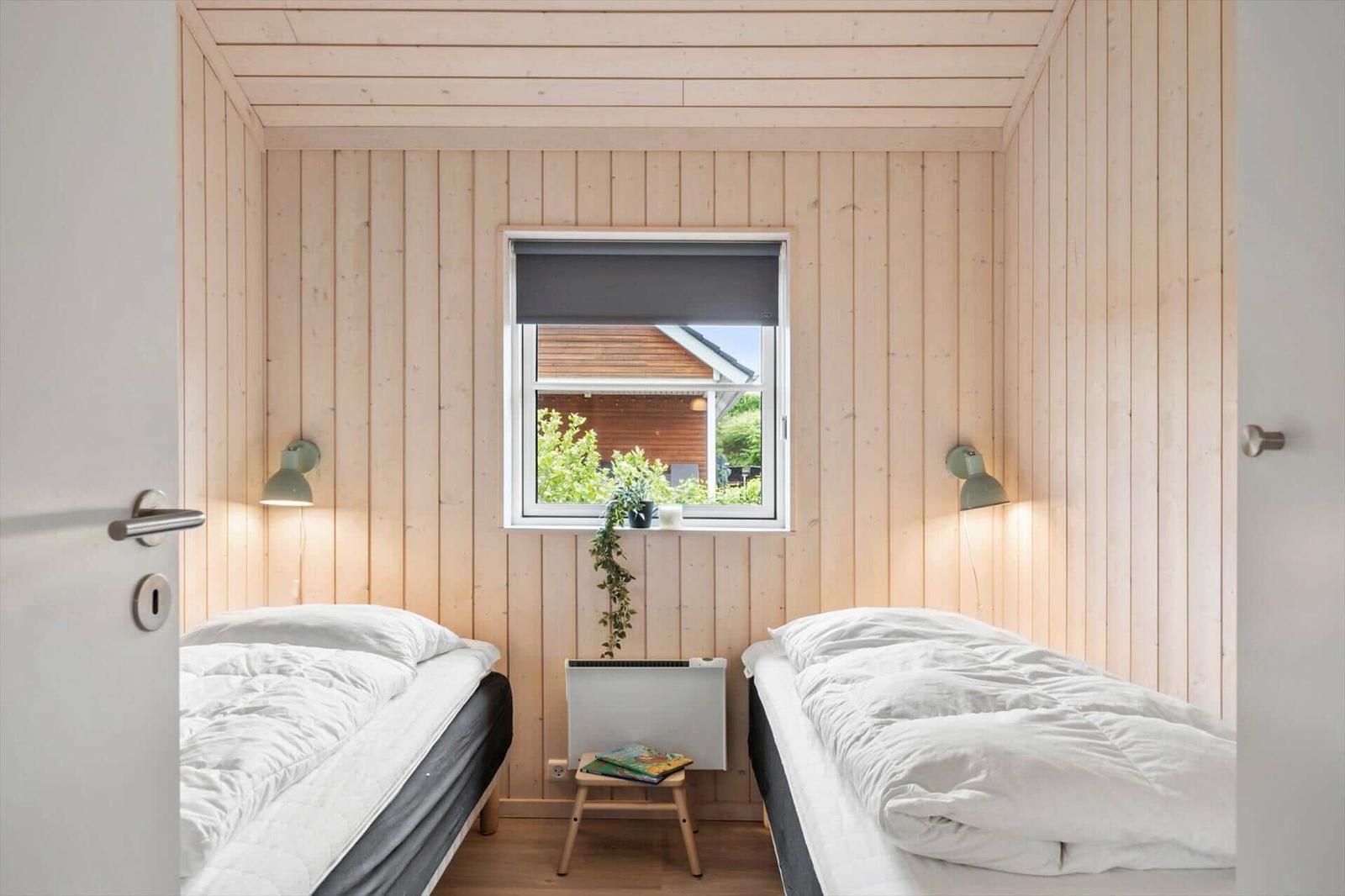 Two beds in a room with wooden walls and a window. A small chair is next to the window.