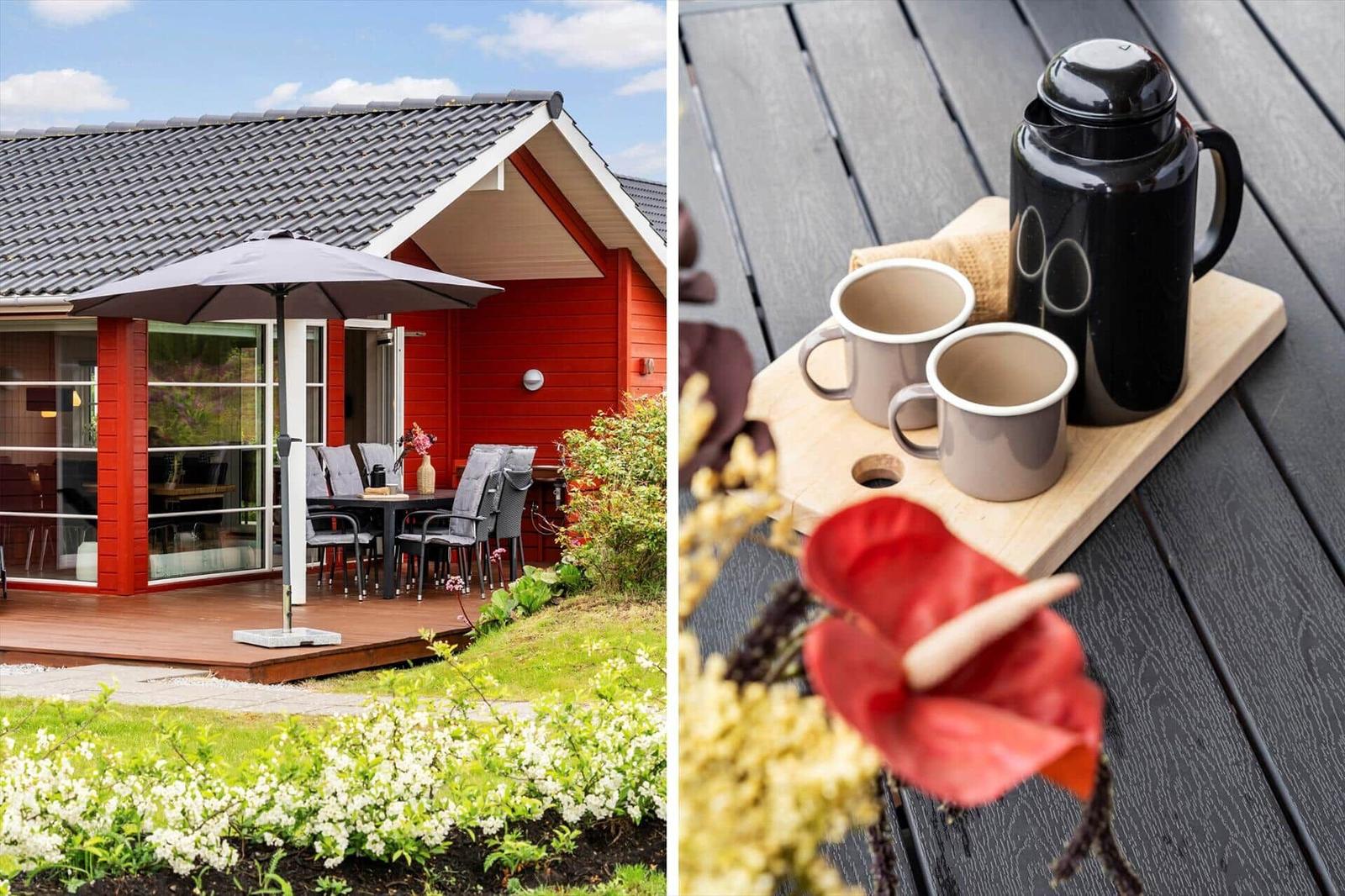 Red vacation house with terrace and garden. On the table are two mugs and a thermos.