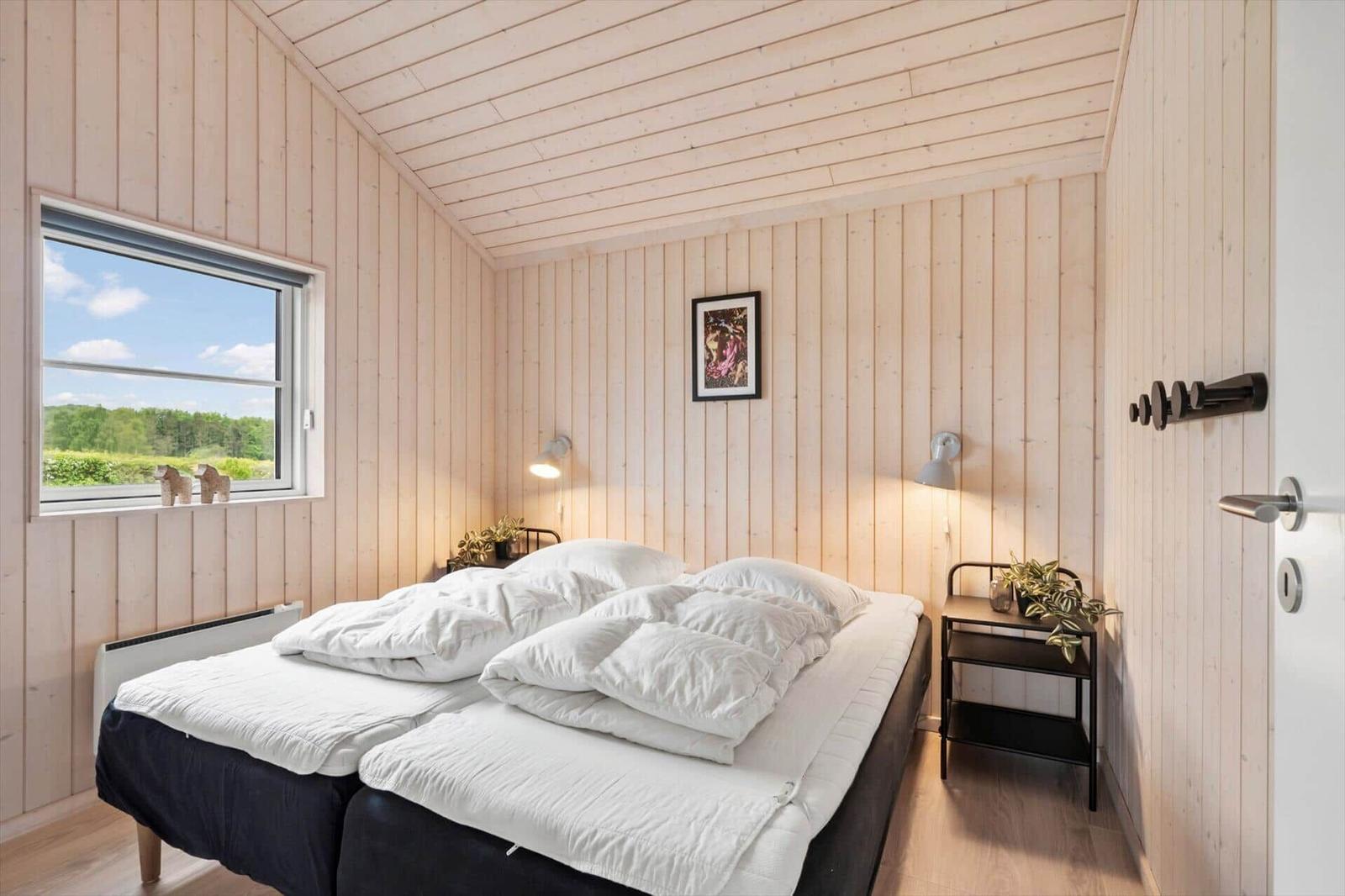 Bedroom with double bed, wood paneling, and window view of landscape.