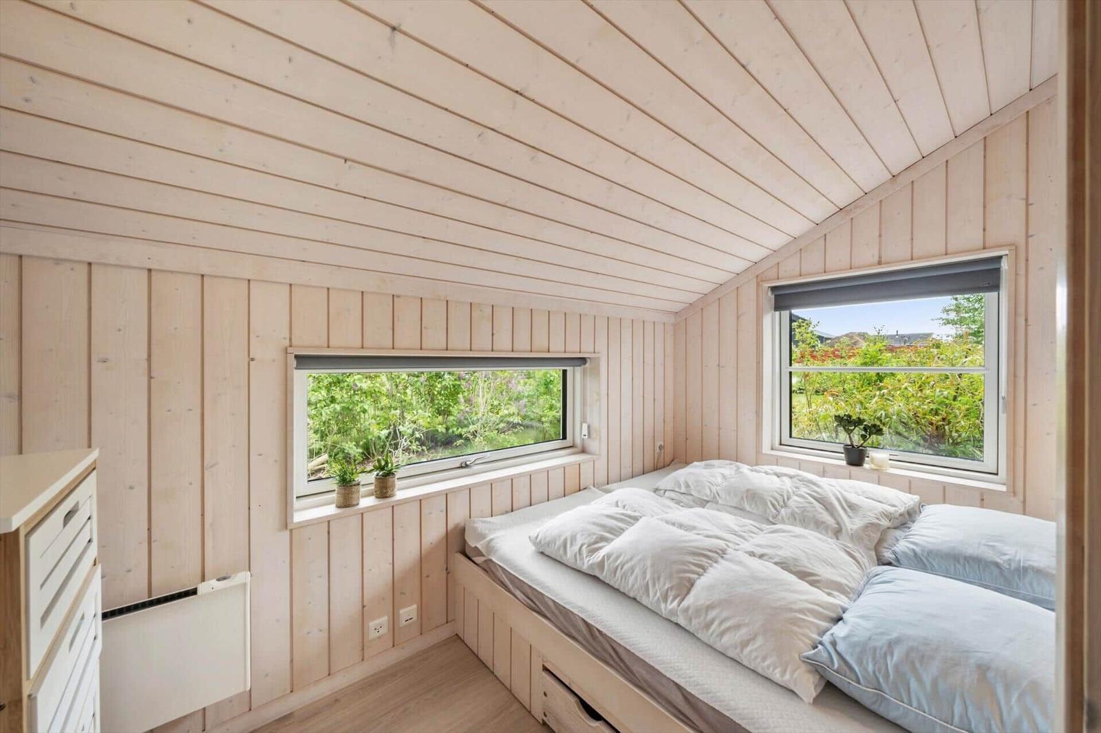 Bedroom with wooden walls, bed, and windows to the garden.