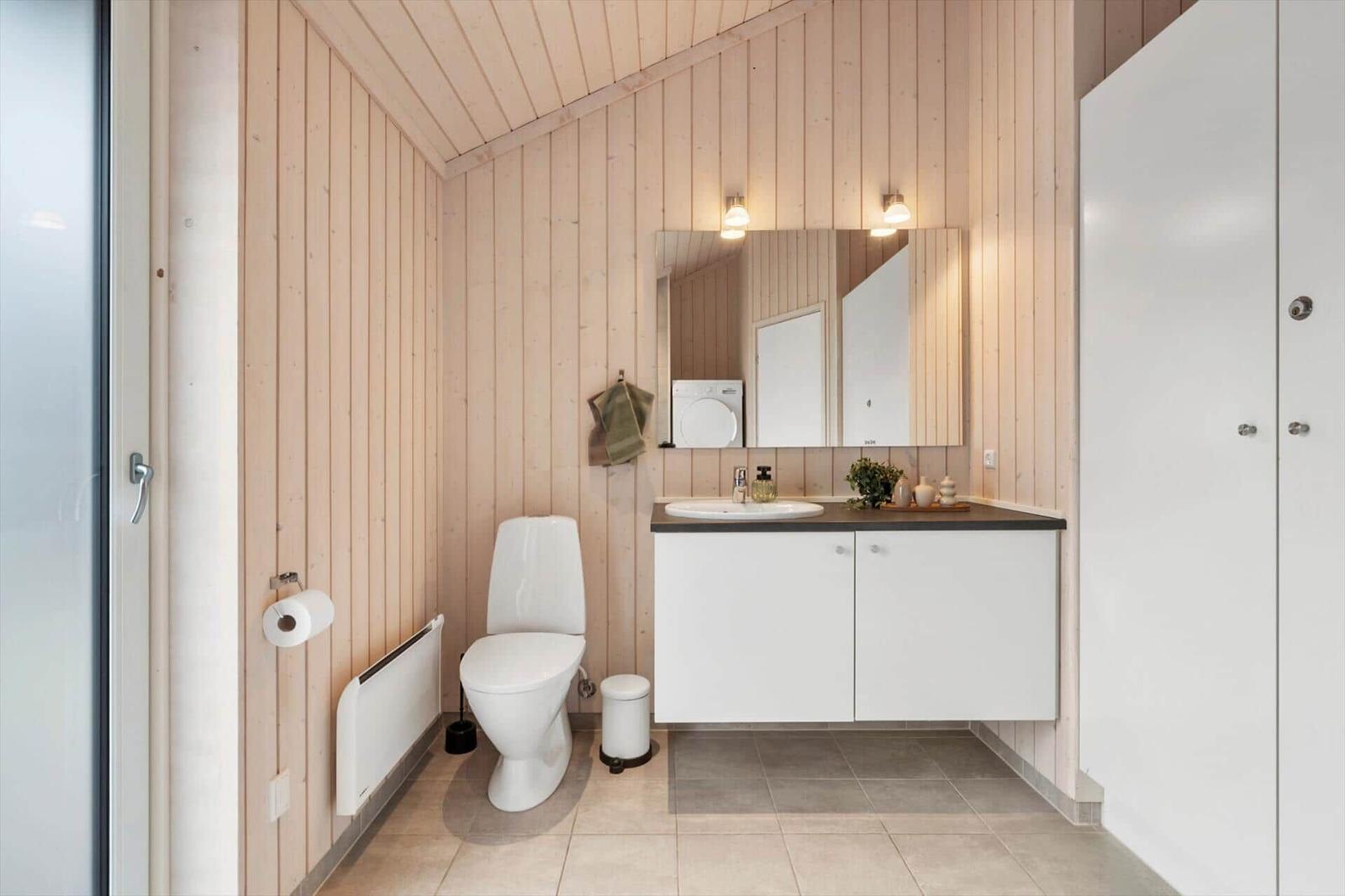 Bathroom with toilet, sink, and mirror on wood wall.