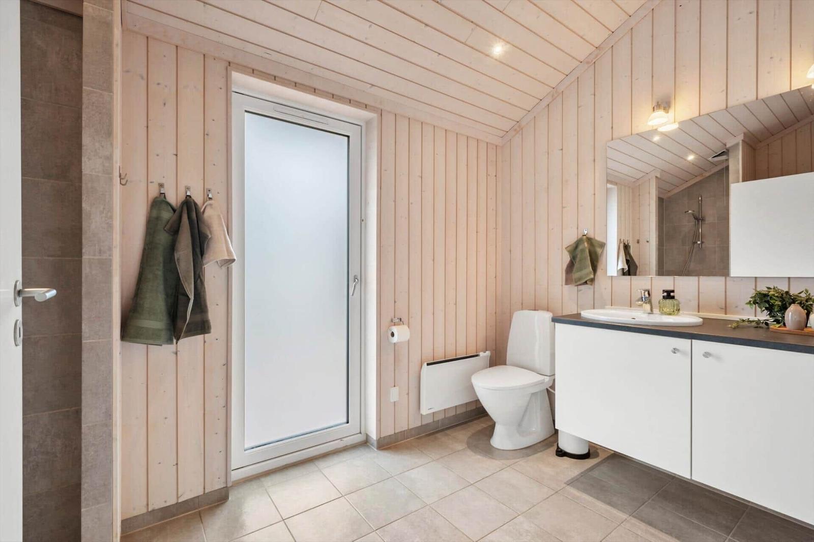 Bathroom with wooden walls, toilet, sink, and shower.