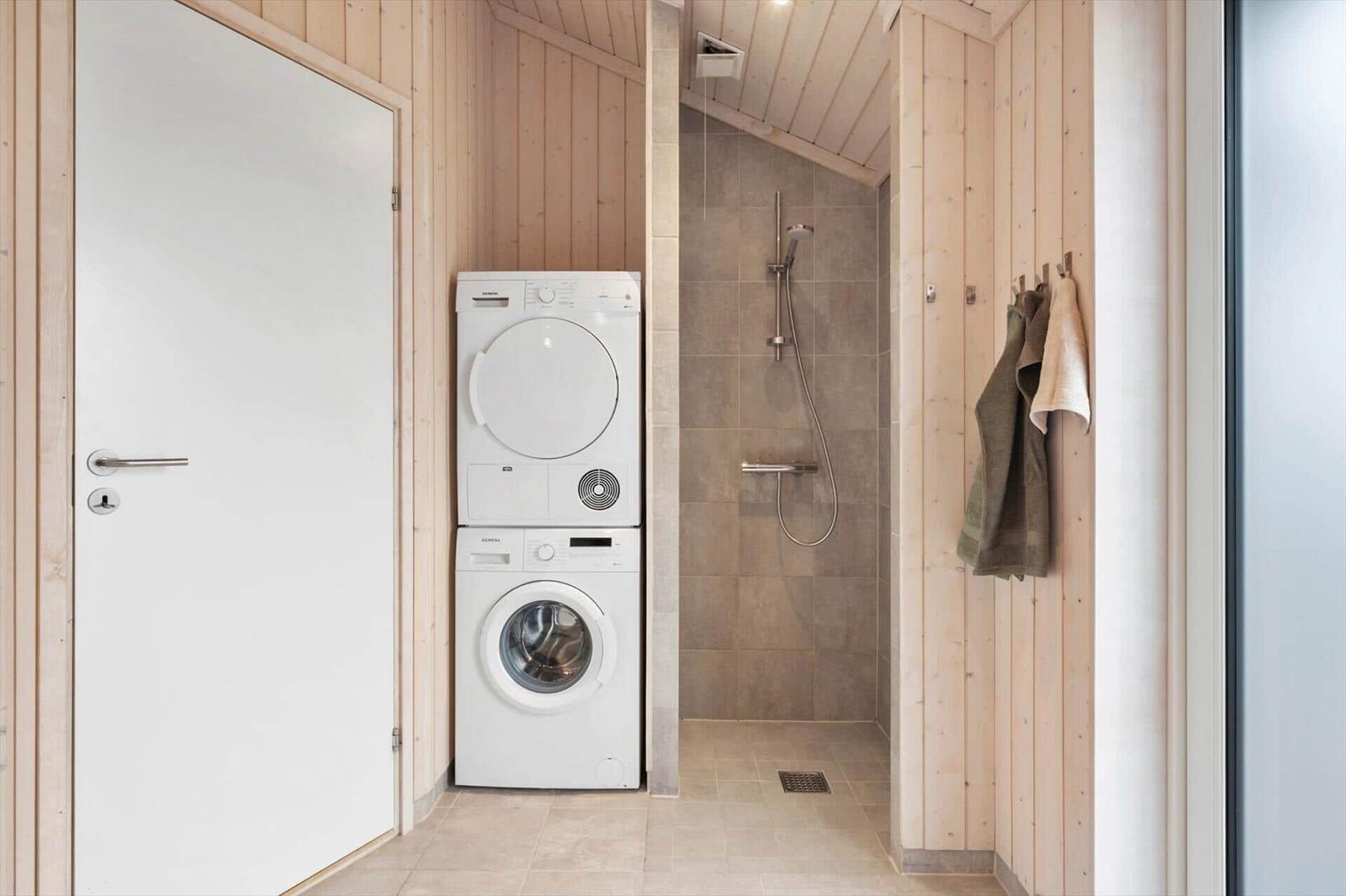 Washing machine and dryer in laundry room next to shower with wooden wall cladding.