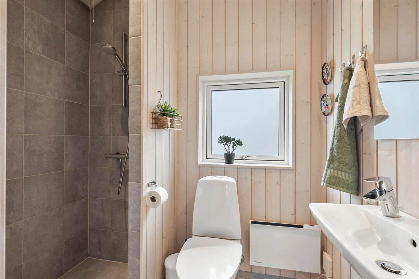 Bathroom with shower, toilet, and sink. Wooden wall, window, and towels.