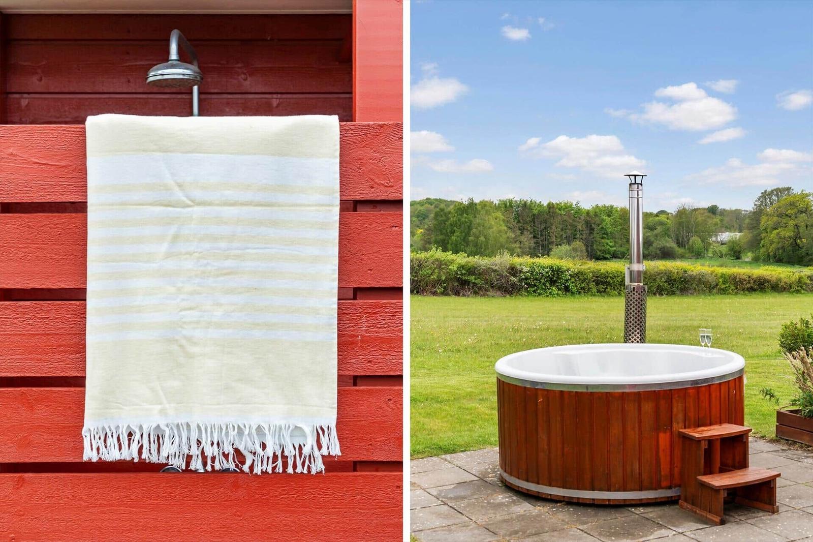Outdoor shower with towel on red wood wall. Hot tub with wooden frame on terrace.