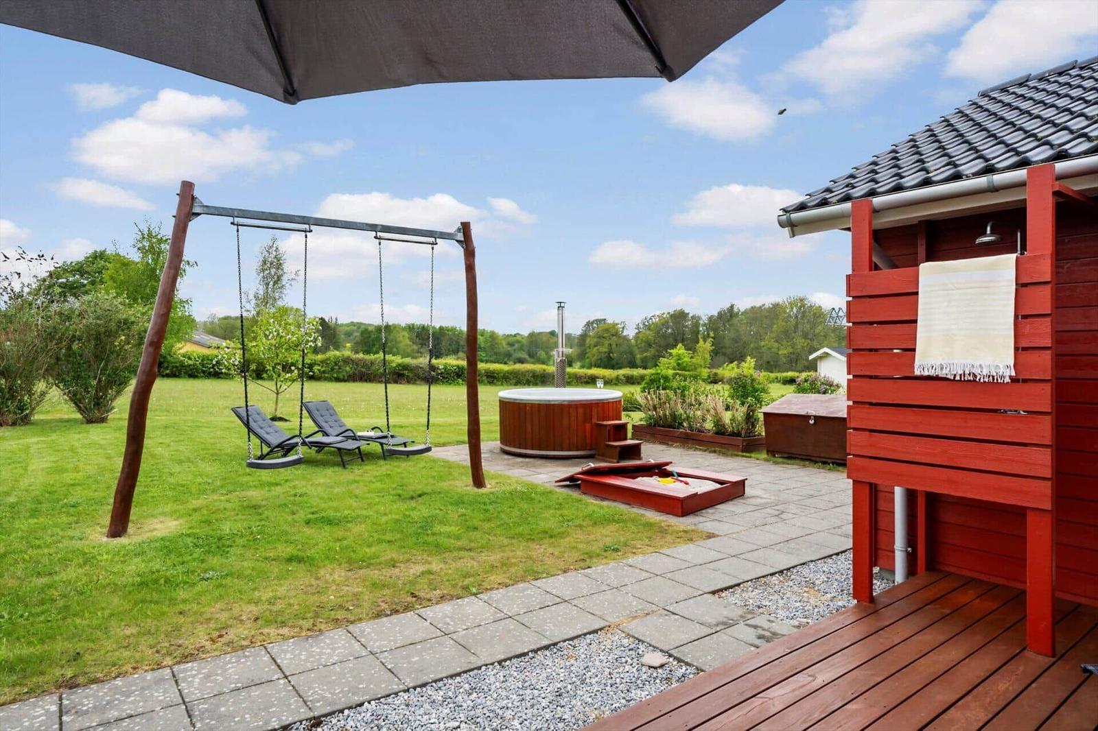 Backyard with hot tub, swing, and terrace. Red wooden structure with shower facility.