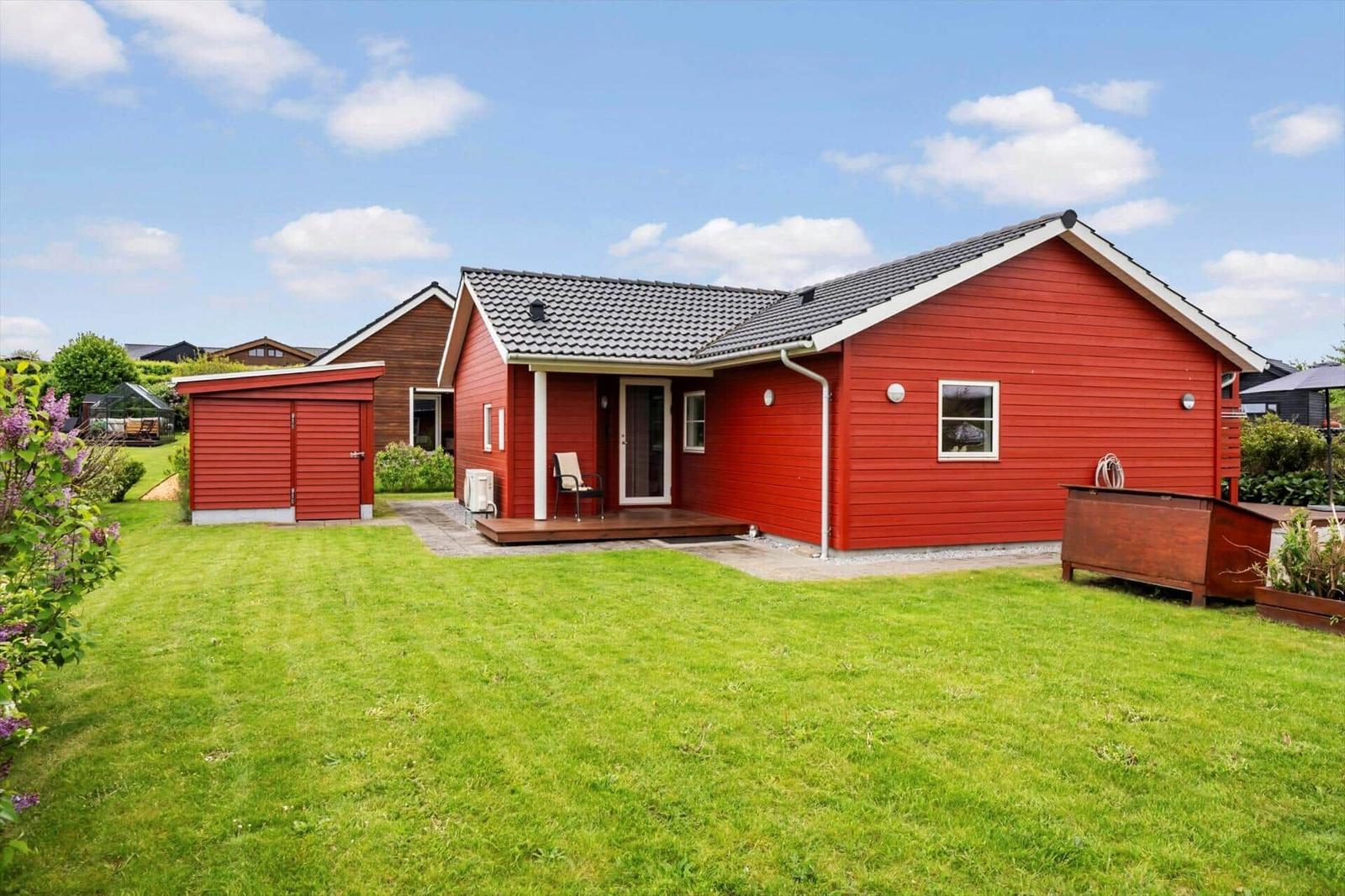 Red house with garden, terrace, and small annex. Background shows other houses.