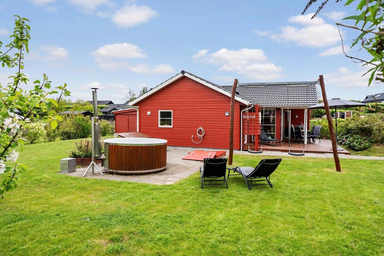 Red holiday home with hot tub, lounge chairs, and terrace in the garden.