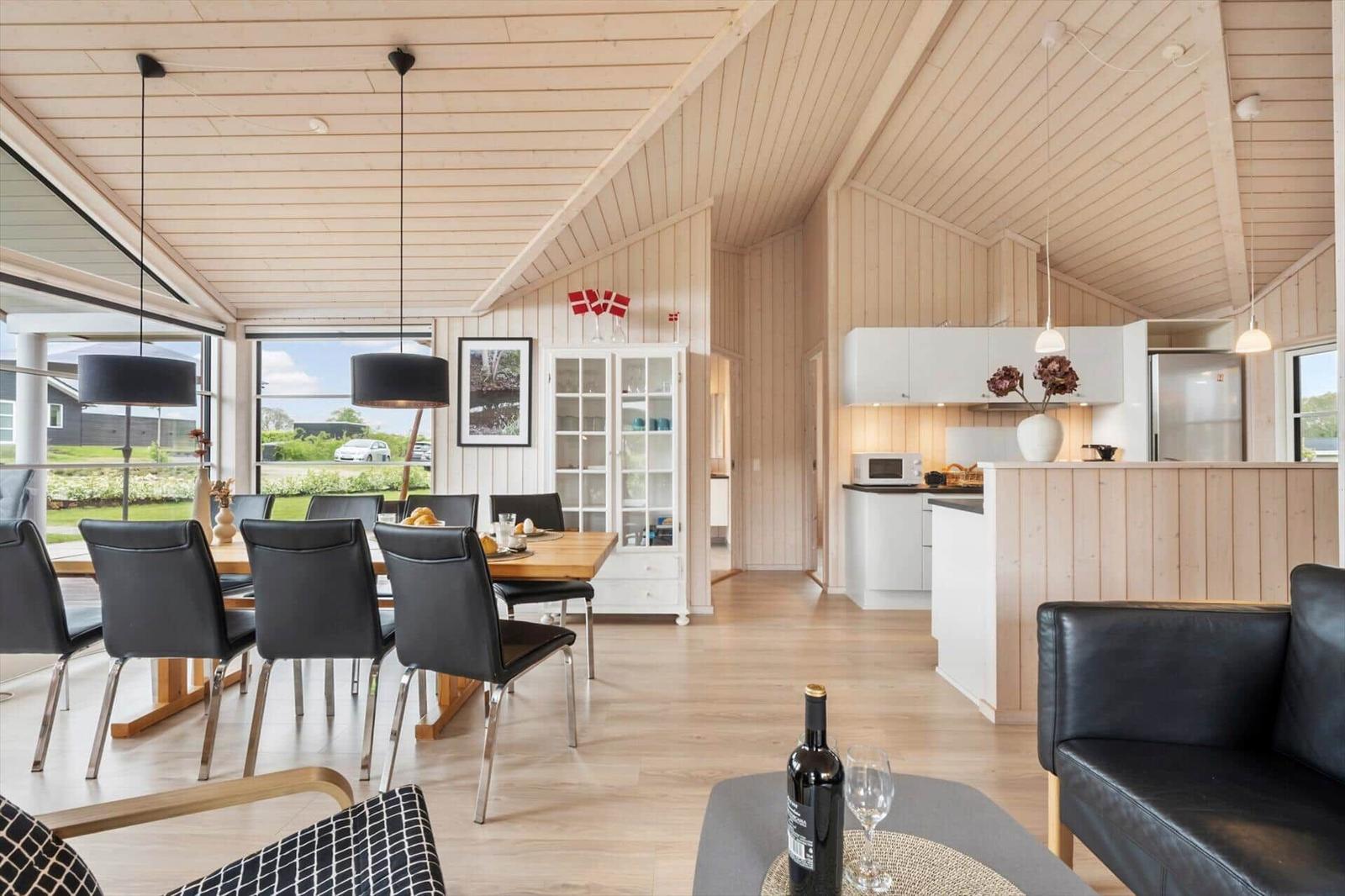 Modern kitchen and dining area with wooden walls and black chairs.