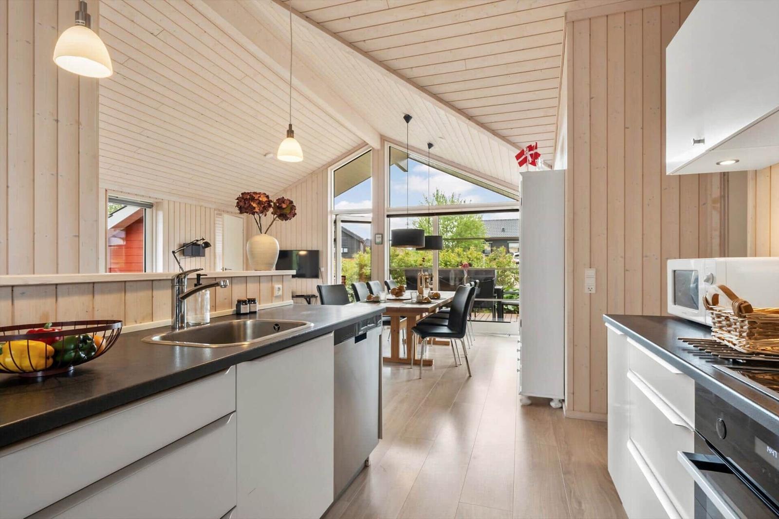 Kitchen with dining area, wooden walls, and large window. White cabinets, black countertop.