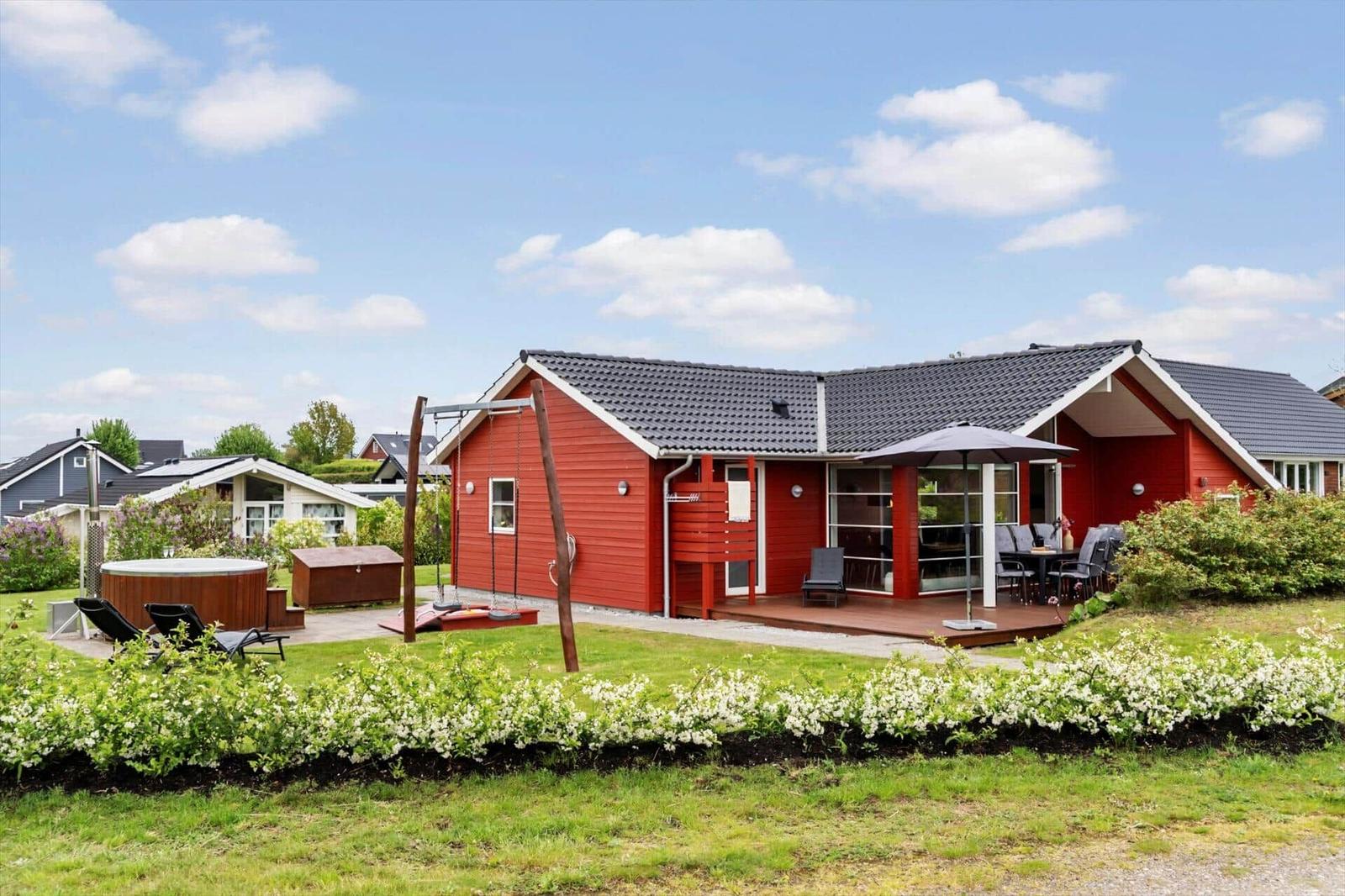 Red vacation home with terrace, garden, and hot tub under blue sky.