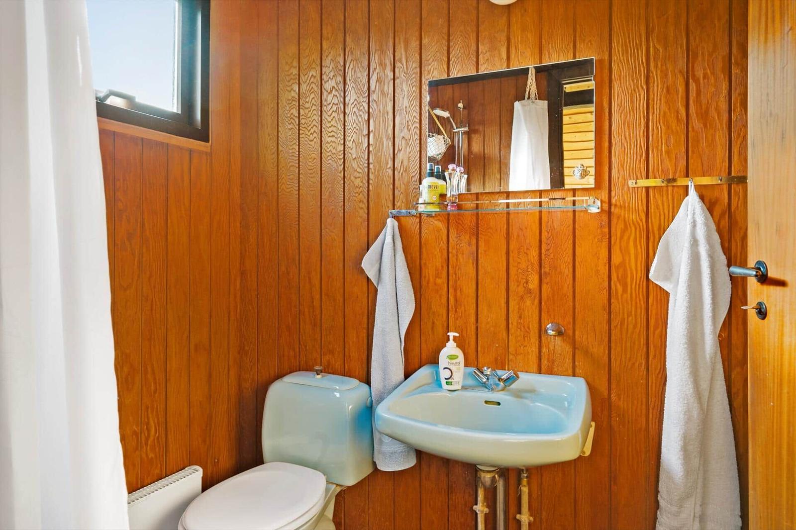 Badezimmer mit Holzwand, Waschbecken, Toilette und Spiegel