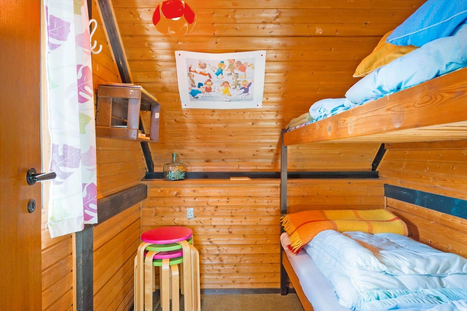 Zimmer mit Holzwand, Doppelstockbett und bunten Stühlen