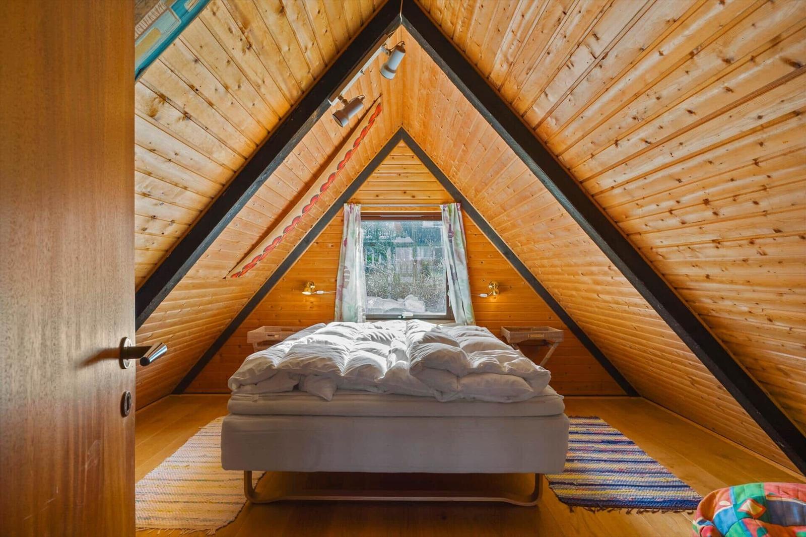 Schlafzimmer mit Holzwand und Dachfenster. Bett mit weißer Bettwäsche.