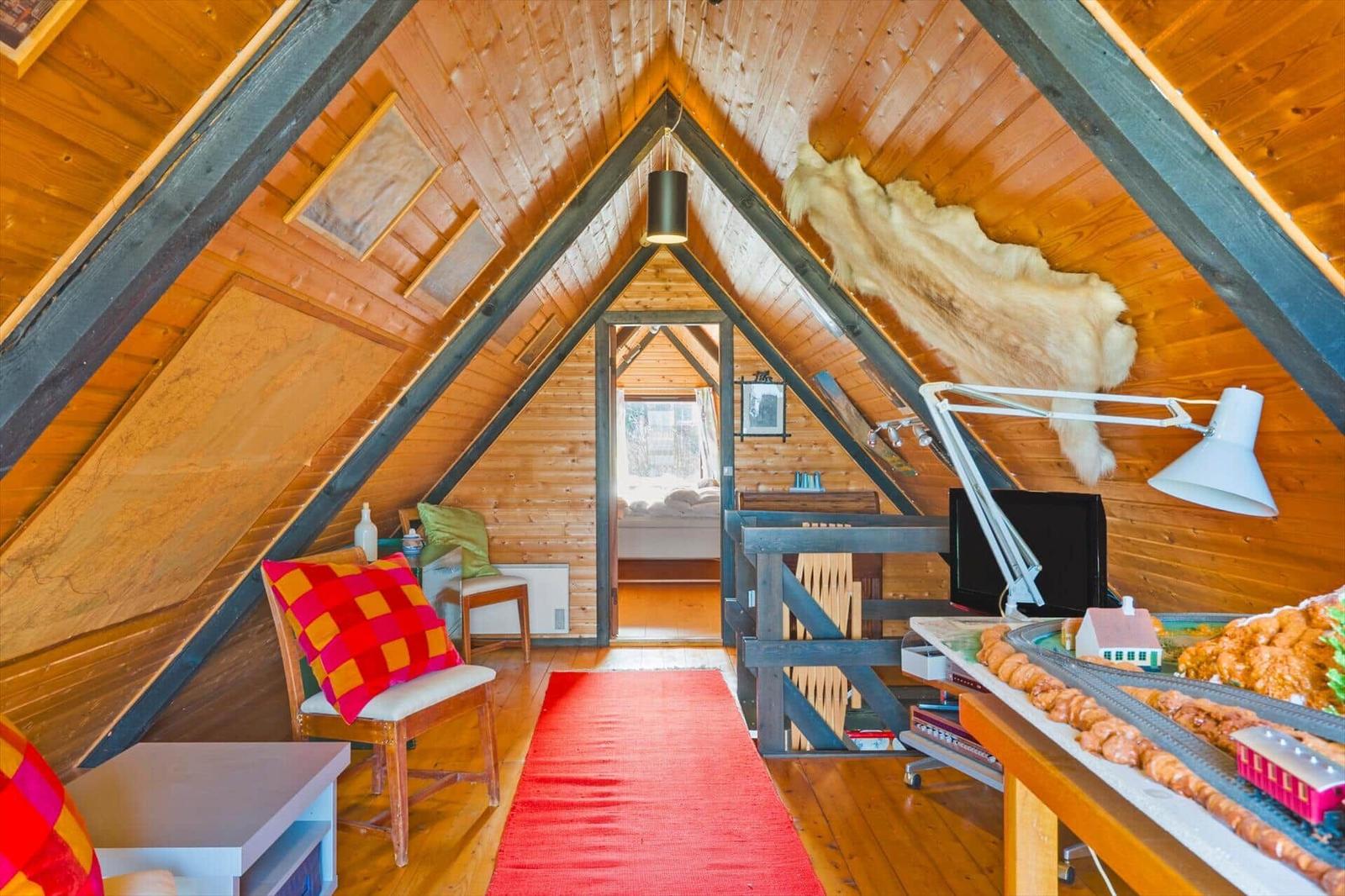 Dachgeschosszimmer mit Holzwand, rotem Teppich und Modellbahn auf Tisch