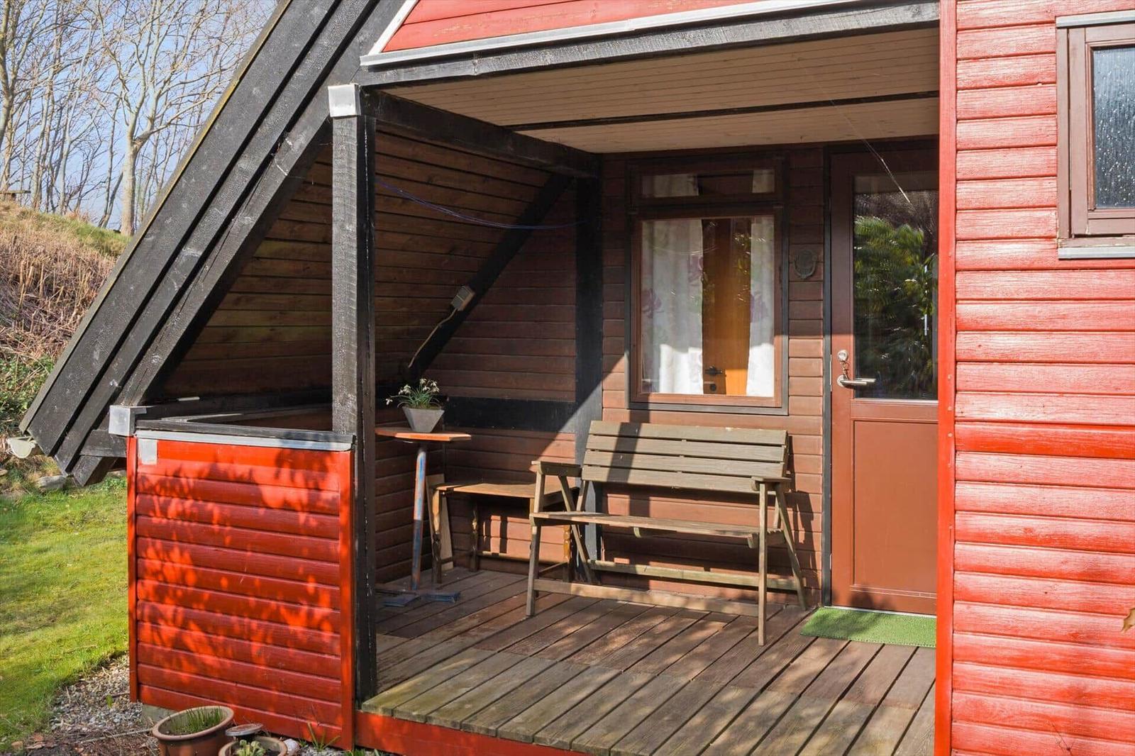 Roter Holzausbau mit Terrasse, Bank und Tisch. Tür und Fenster sind sichtbar.
