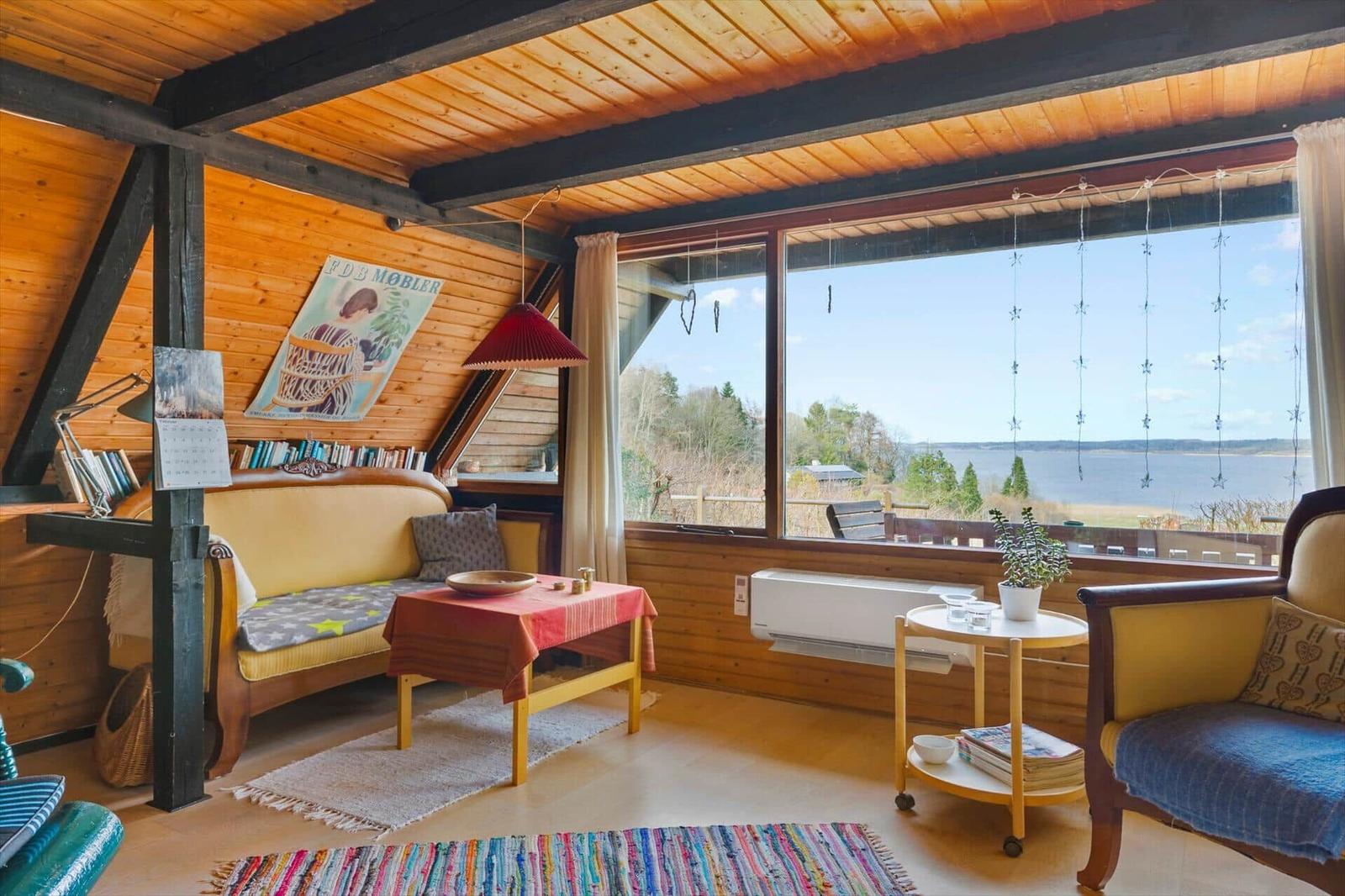 Wohnzimmer mit Holzdecke und großem Fenster zum See