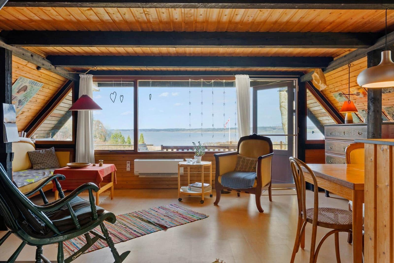 Wohnraum mit Holzdecke und Blick auf Wasser. Möbel und Einrichtung sichtbar.