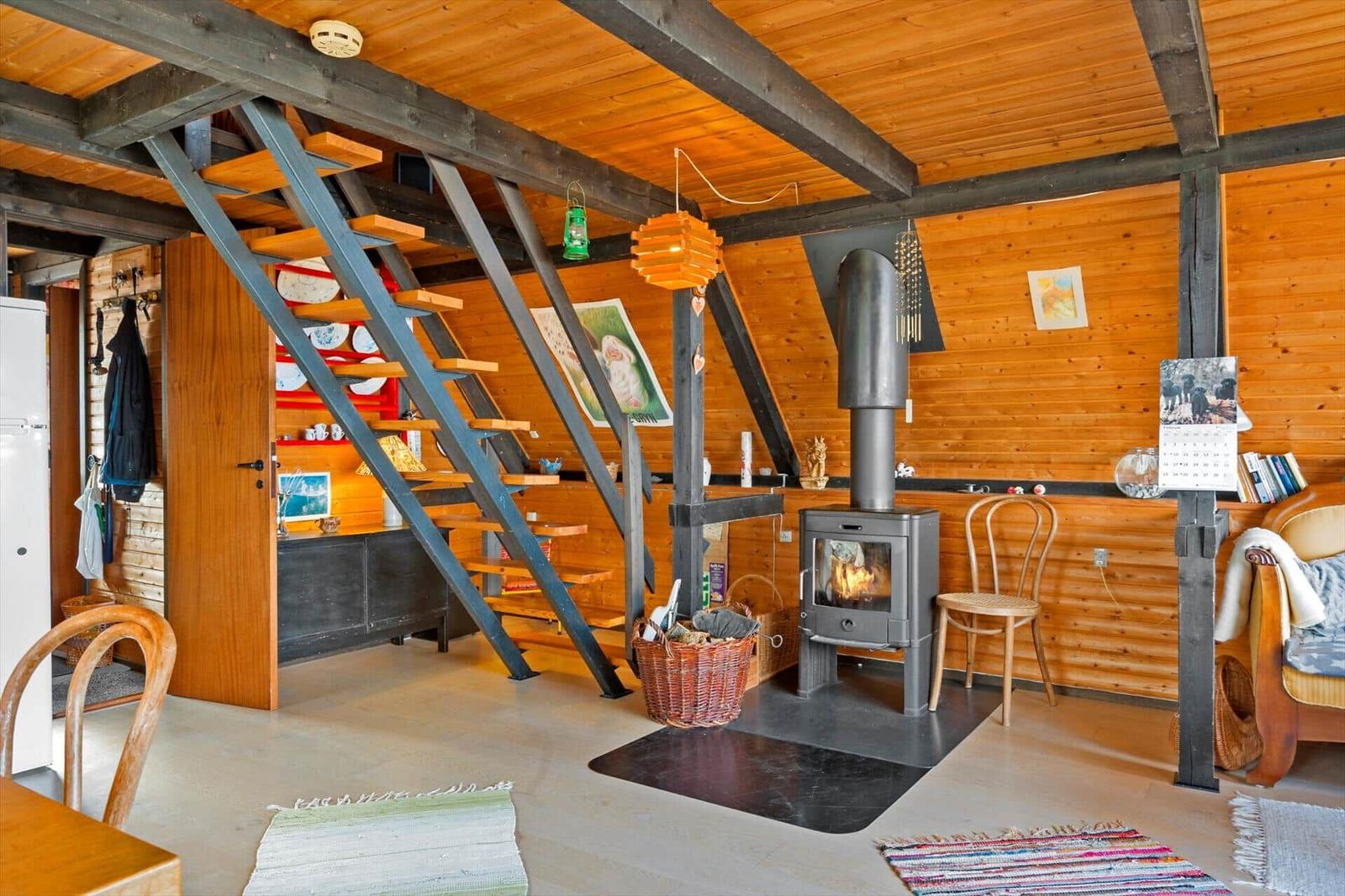 Wohnraum mit Kamin, Holzwand und Treppe zur oberen Etage.