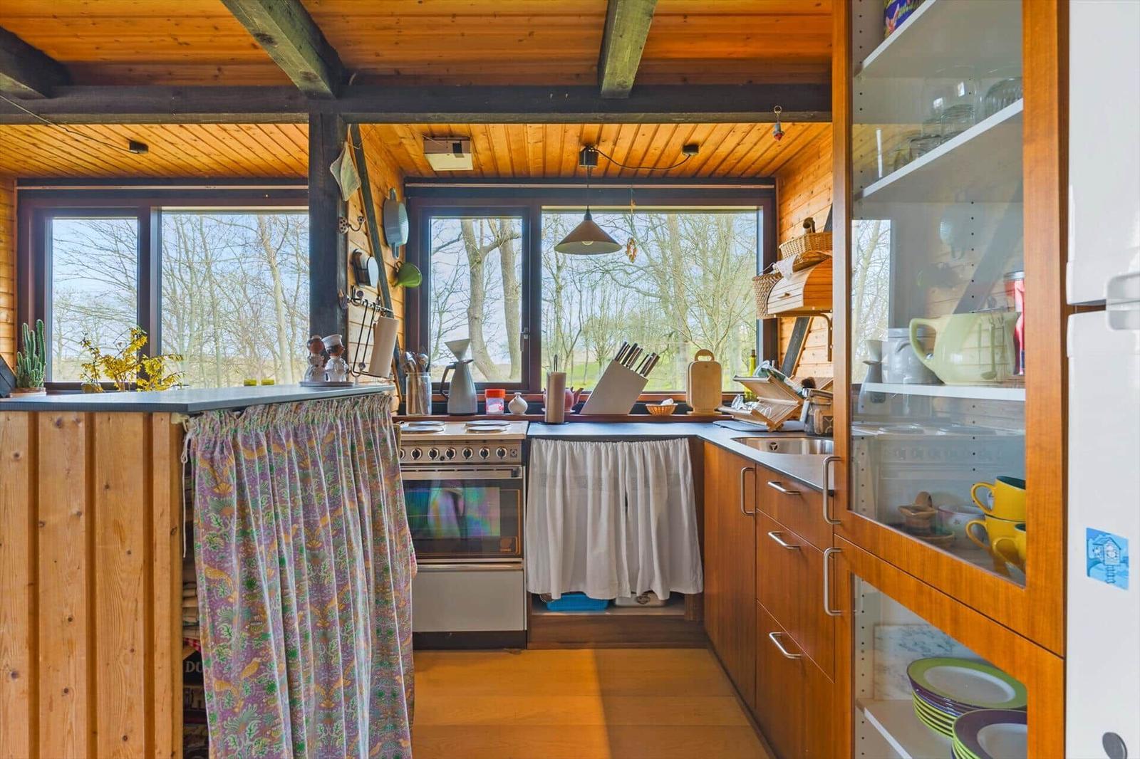 Küche mit Holzdecke, Fenstern und Küchenzeile mit Geschirr und Kochutensilien.