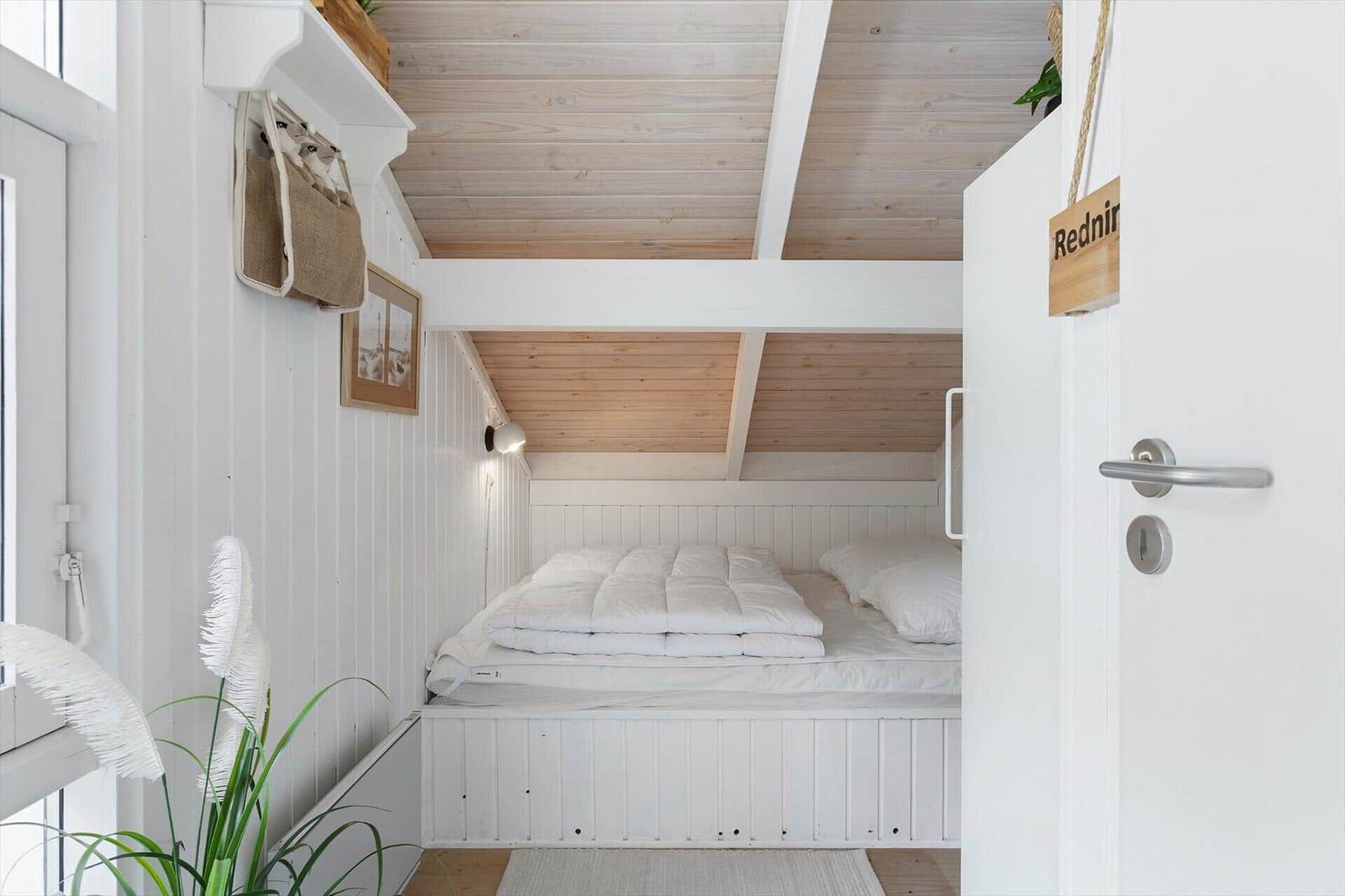 Bedroom with white bed, wooden ceiling, and door with sign.