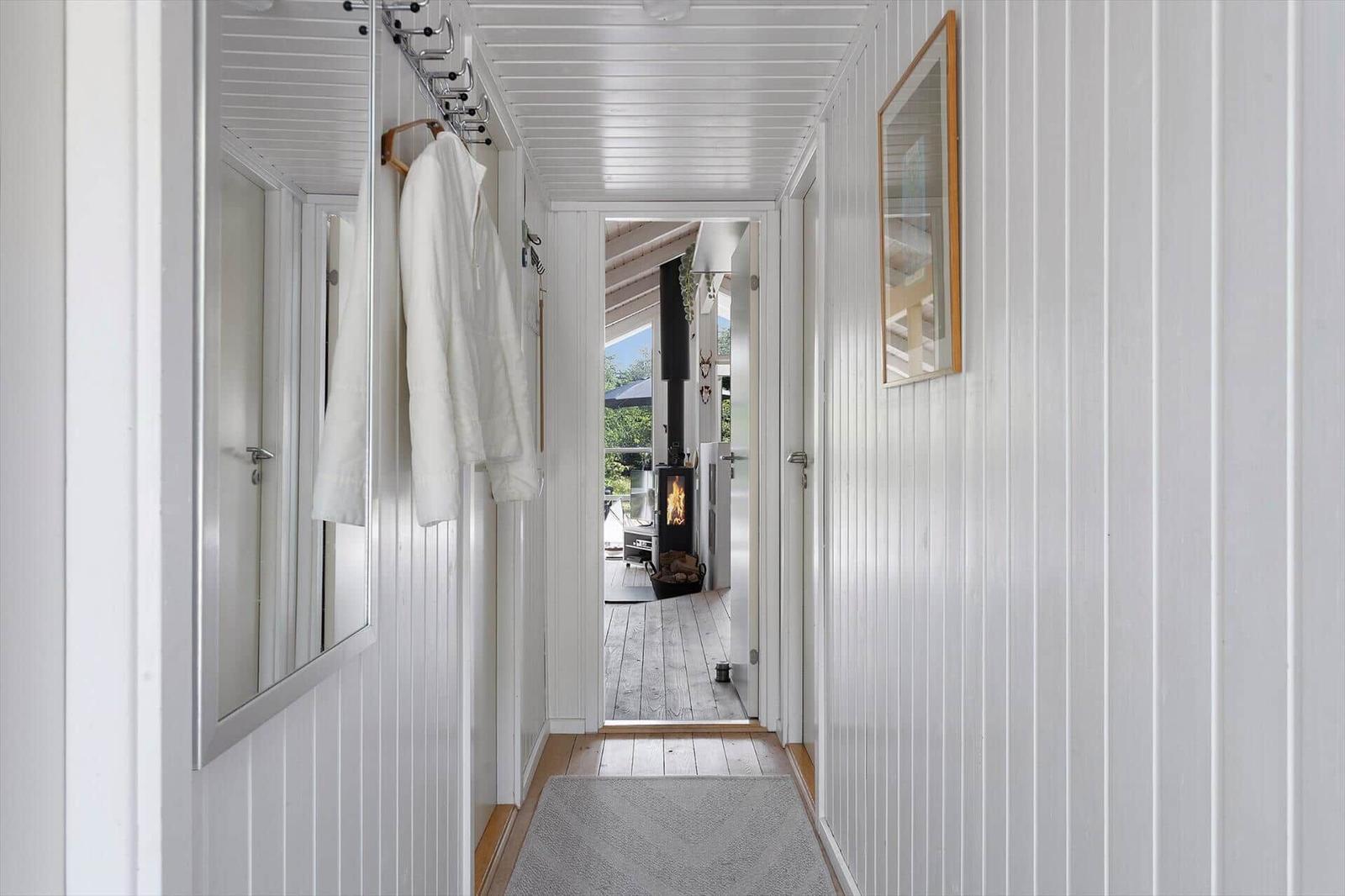 Hallway with white walls, mirror, and robe. Passage to living area with fireplace.