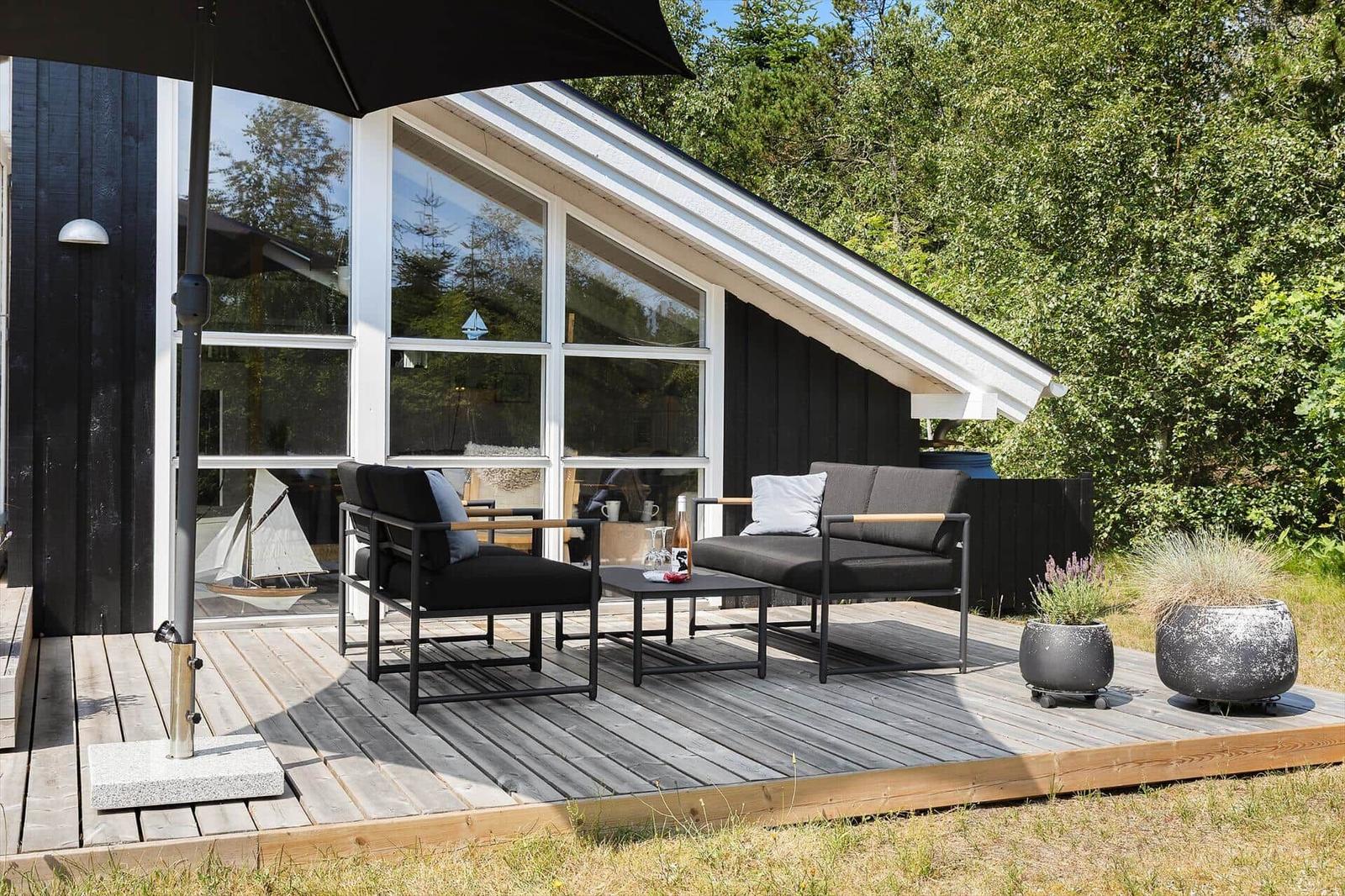 Deck with seating, umbrella, and plants in front of a house with large windows.