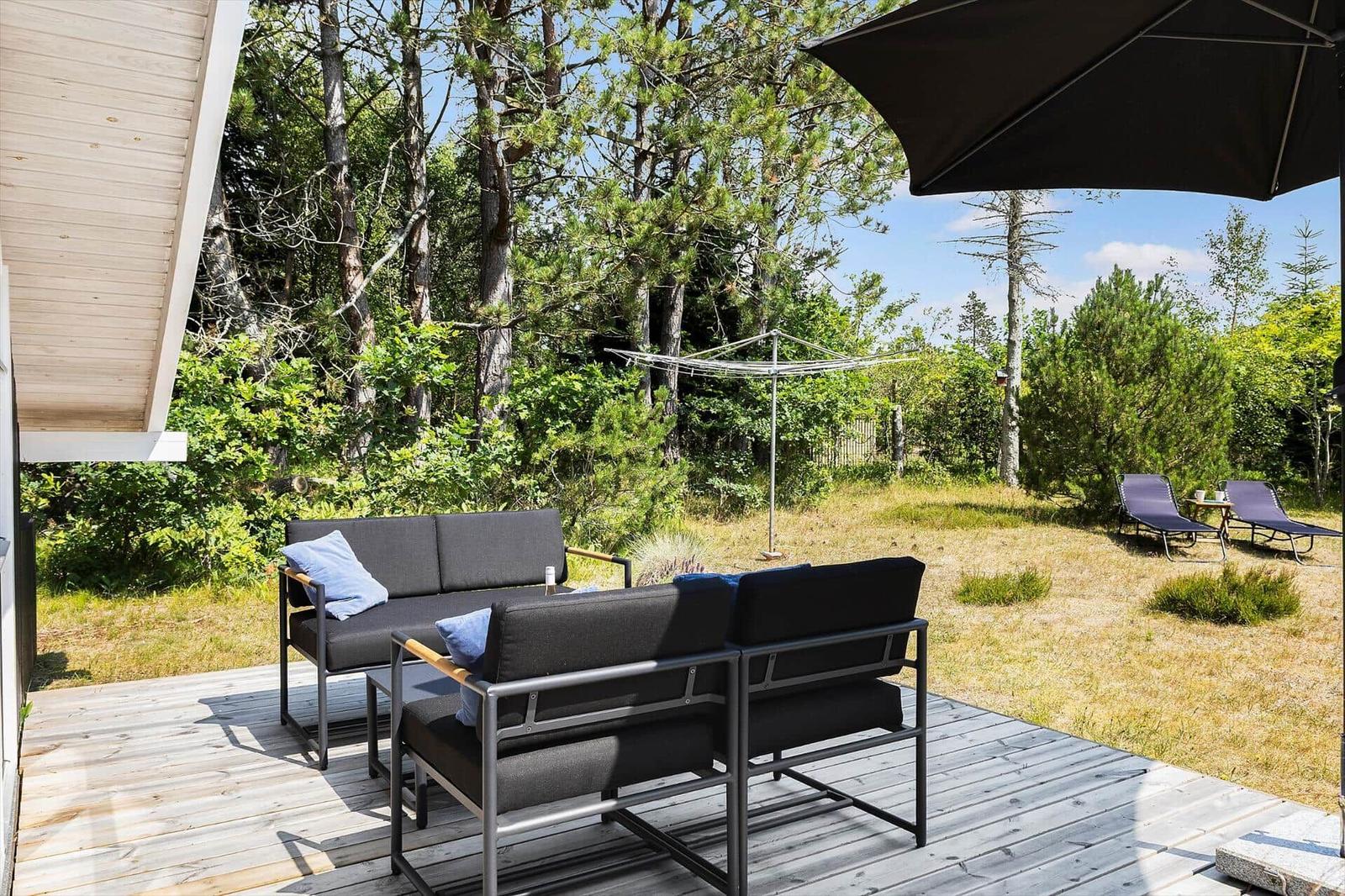 Deck with seating group, umbrella, and lounge chairs in green area.