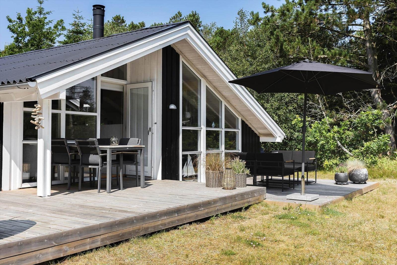 Modern wooden cabin with large balcony and outdoor seating area under umbrella.