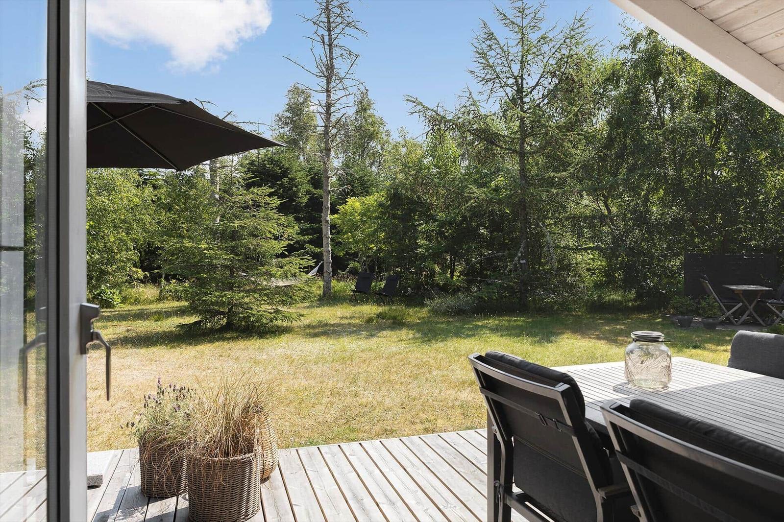 Deck with table, chairs, and umbrella. Lawn and trees in the background.