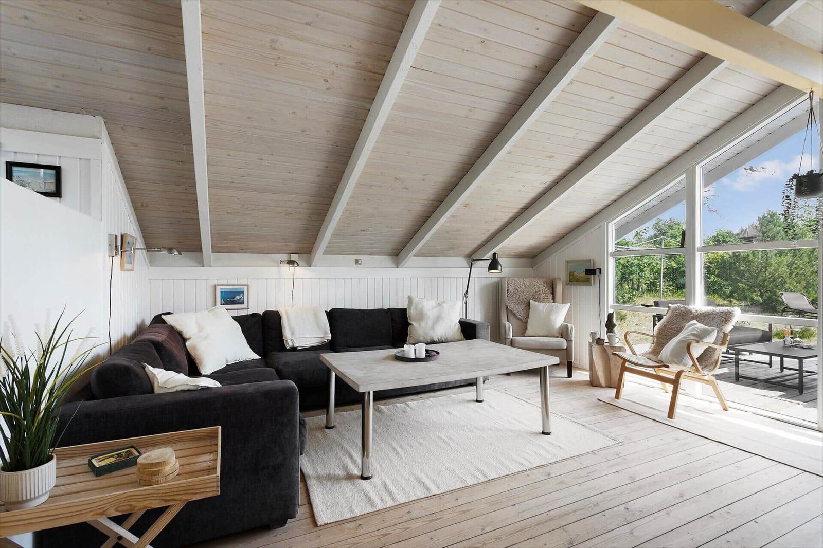 Living room with sofa, table, and chair under wooden ceiling with garden view.
